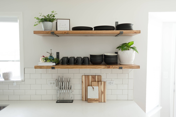 open shelving in a kitchen on a white wall with windows on the side