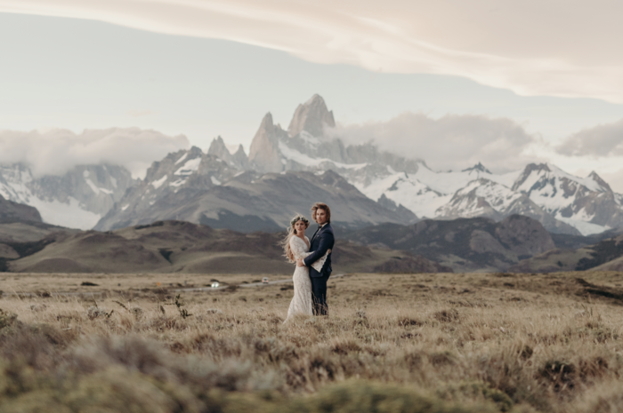 wedding picture of a couple in the middle of a field with snowy peaks in the background