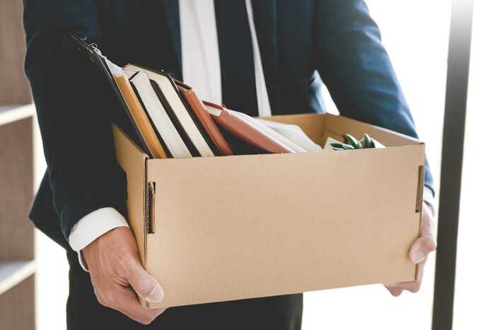 man in a suit resigning from work with a large cardboard box full of journals and text books