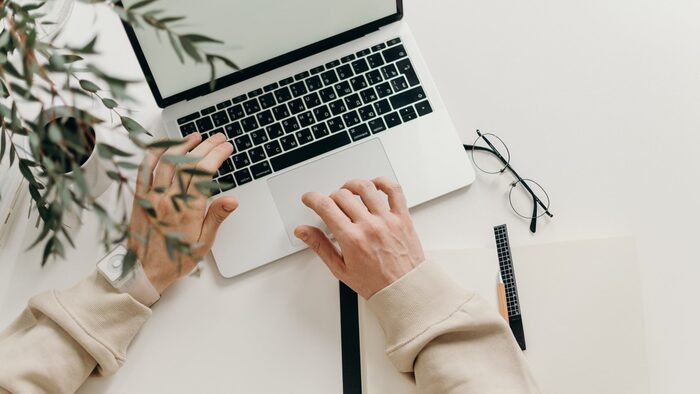 person working on a laptop with a cup of coffee and glasses on the side with branches of green leaves