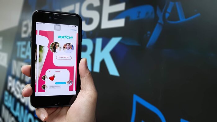 a hand holding a smart phone on a black wall with a dating site opened on the screen