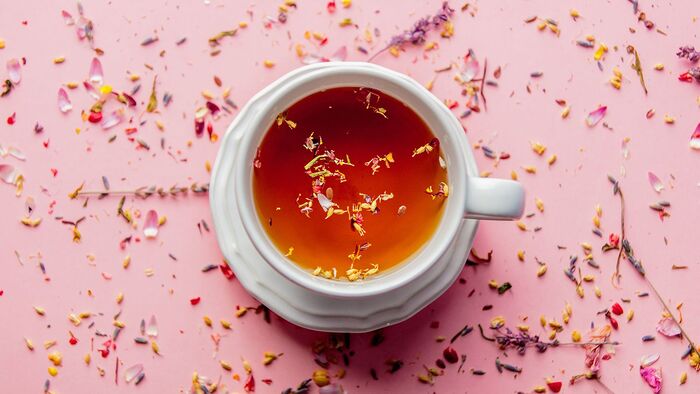 effects of tea a white tea cup sprinkled with herbs on a pink background 