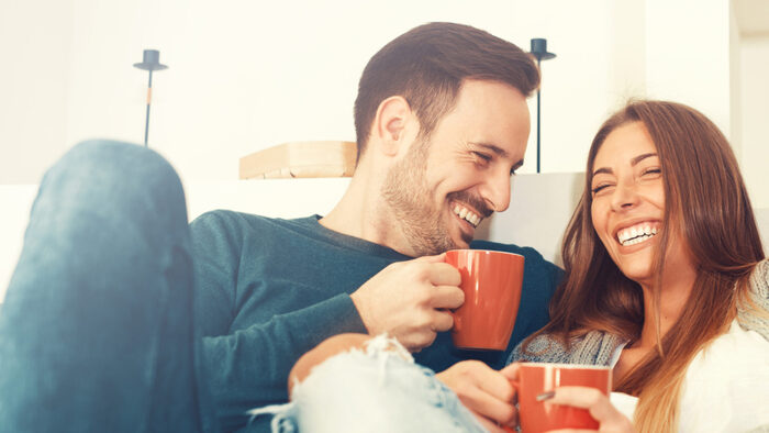 Couple in love cuddling and smiling holding red mugs
