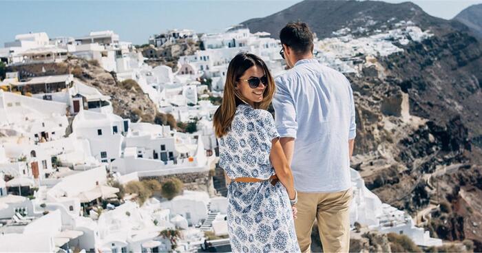 couple walking in Santorini overlooking the caldera with a woman looking back smiling