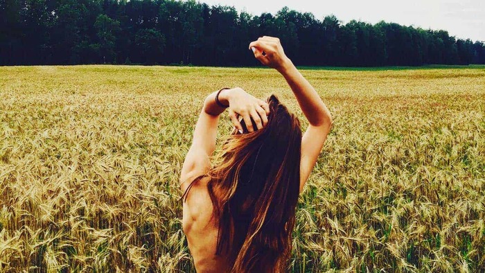 back of a naked woman in the middle of a wheat field holding her hair back 