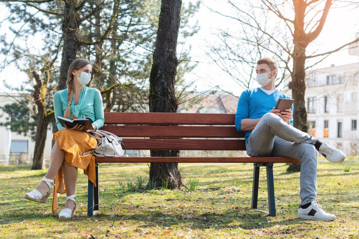 social distancing a couple sitting on the two ends of a bench with their masks on and books in their hands