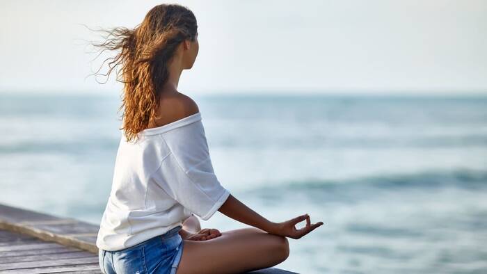woman with jeans shorts and white t-shirt sitting on a wooden peer meditating with the wind in her hair