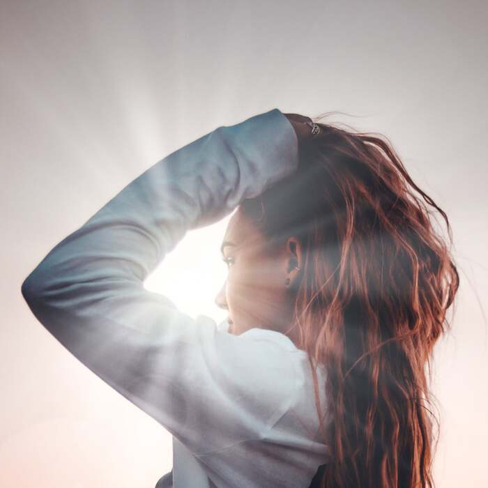woman in white shirt standing against the sunlight touching her hair and lifting it