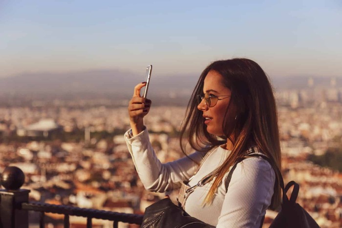 woman with sunglasses at a high place taking pictures on her phone travelling solo 