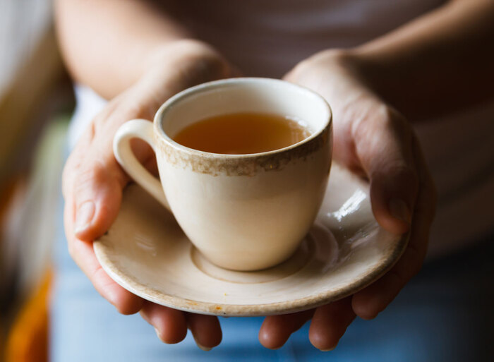 woman holding a small tea cup in her two hands and bringing it close to the photo camera