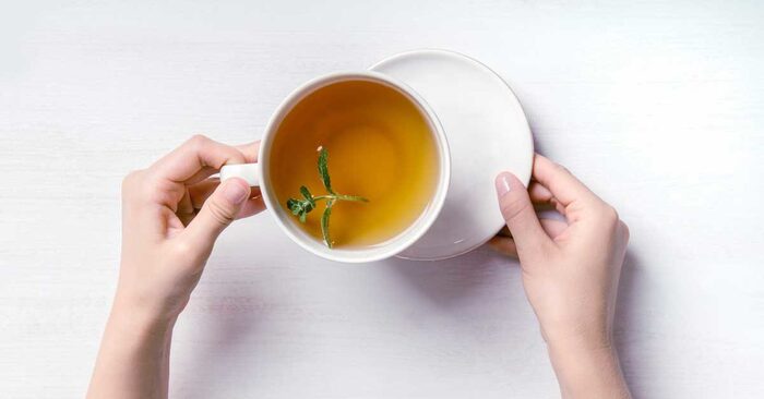 tea for upset stomach two hands holding a white cup of tea on a white background