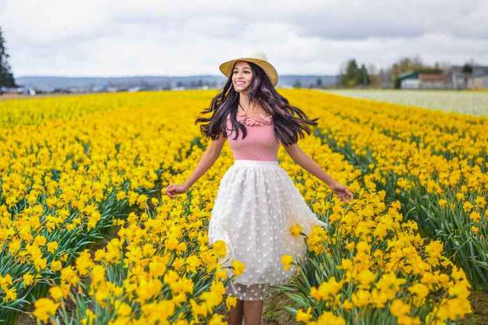skagit valley girl with long black hair white skirt pink top and a sun hat in a field of blooming yellow flowers