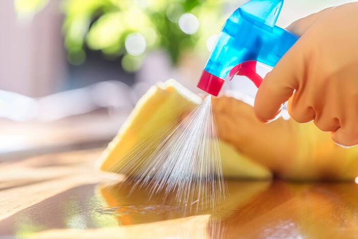 two hands in yellow rubber gloves cleaning a wooden surface with a cleaning spray and a yellow towel