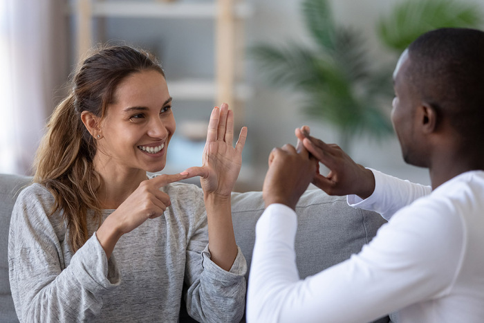 man and a woman sitting on a couch communicating with hand gestures and signs