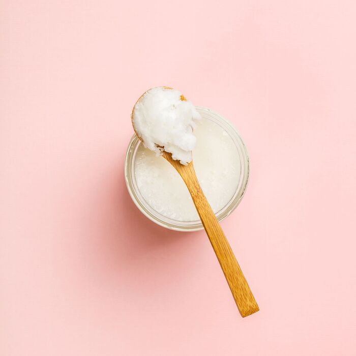 a jar with white hair mask and a wooden spoon on a light pink background