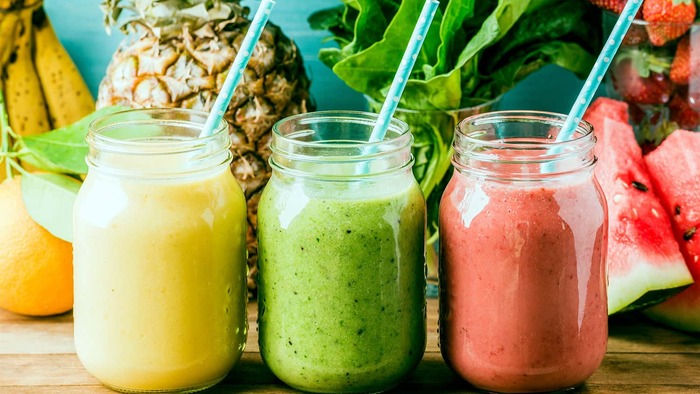 three detox juices in glass jars with colorful straws and fruits in the background