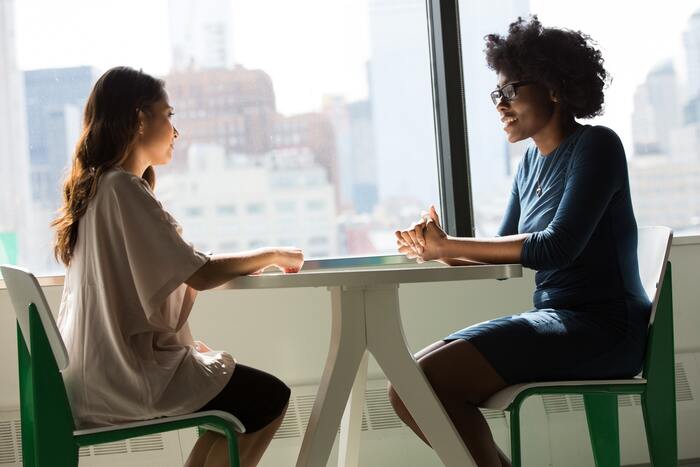 effective communication two women sitting across a table in front of a large window talking