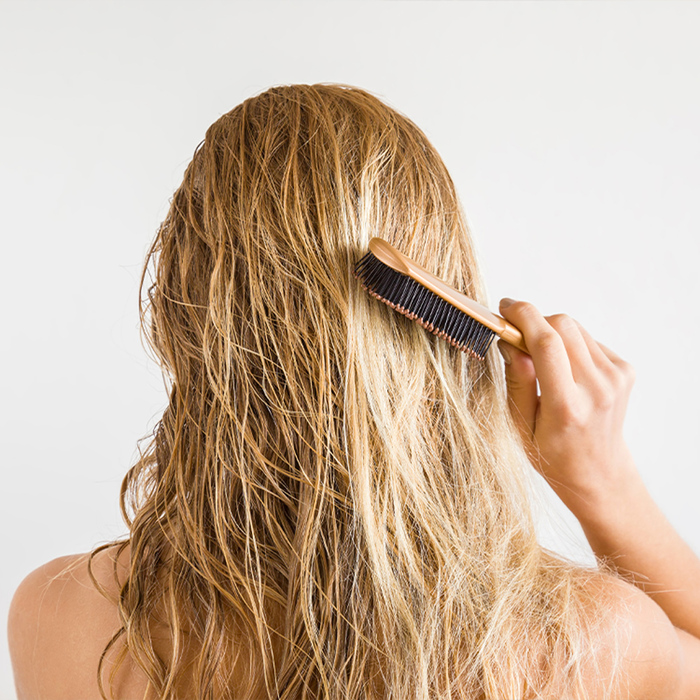 the back of a woman with blond hair brushing through her wet hair 