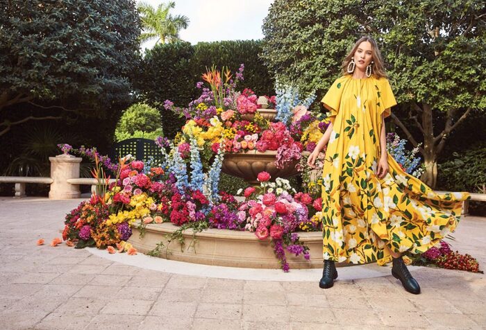 woman in yellow floral dress in front of a flower fountain in a large garden