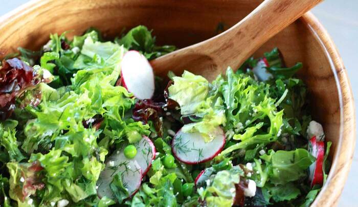 green salad in a large wooden bowl with a wooden spoon