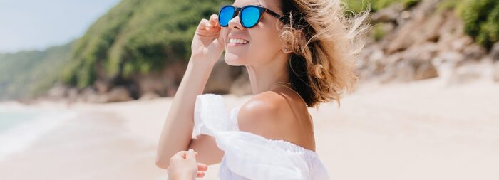 hair protection blond woman on the beach wearing blue glasses smiling and enjoying the sun