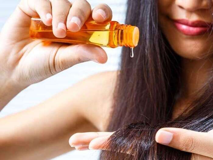 woman with long dark hair applying a hair serum from a yellow bottle on the ends of her hair