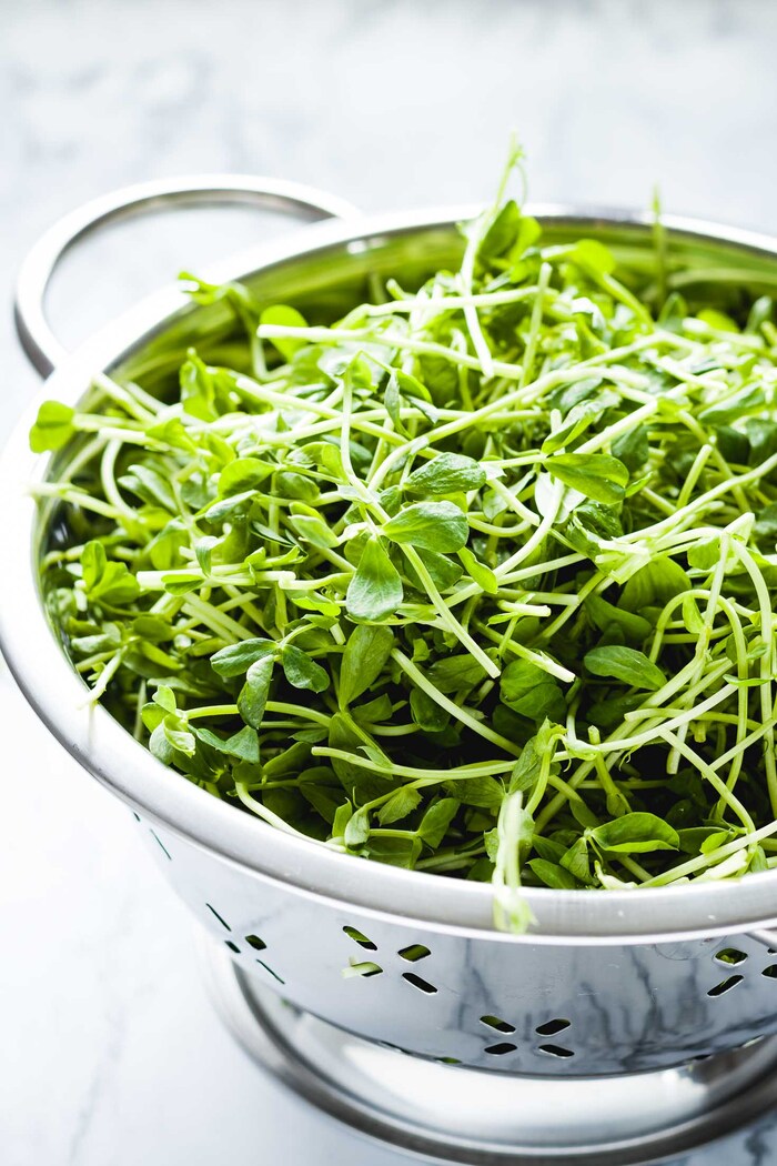 pea shoots in a large metal strainer