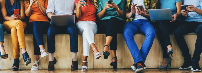 people sitting in a row in colorful clothes communicating via technology holding laptops and mobile phones in their hands