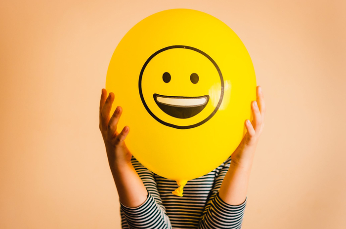 person in a striped shirt holding a large yellow balloon with a smiley face on it