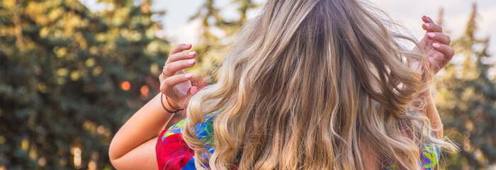 back of a blond woman in a colorful top playing with her hair outdoors