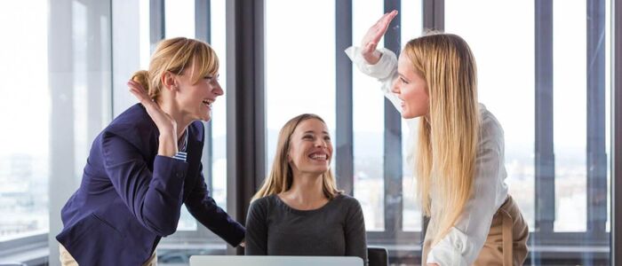 three blond women in an office environment smiling and celebrating success 