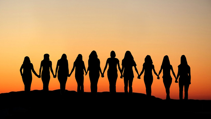 women holding hands walking together towards the sunset 