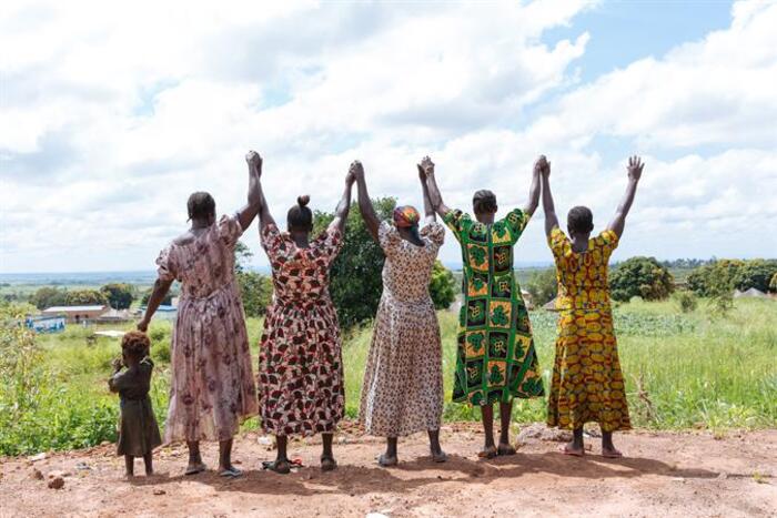 women in uganda in colorful african clothes raising their hands together in nature