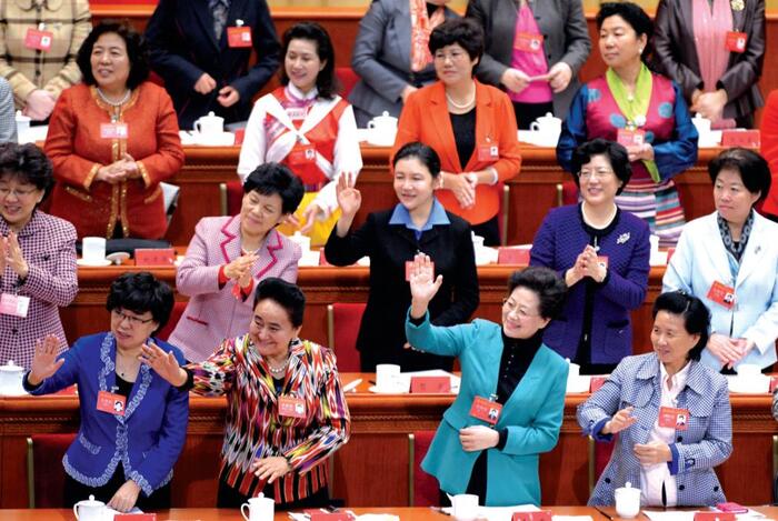 adult women in china dressed in suits in an official setting waiving and smiling