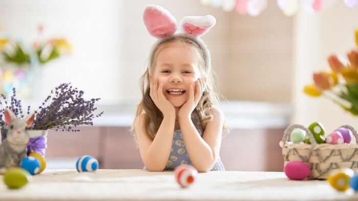 celebrate easter little girl at home smiling at the camera holding her face with two hands surrounded by painted eggs