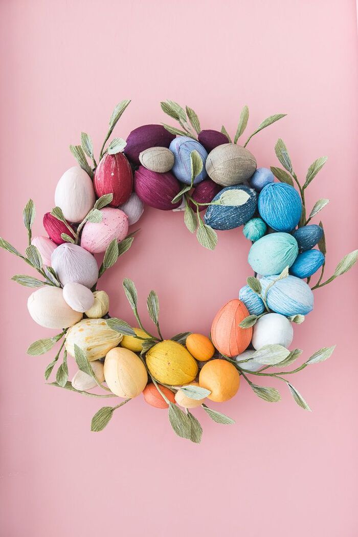 paper wreath with colorful eggs and green leaves on a light pink background