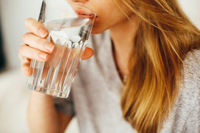 blond woman with grey shirt with a large water glass drinking