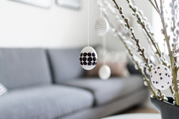 modern easter decor grey sofa in the background and white egg with black dots and triangles hanging from spring branches
