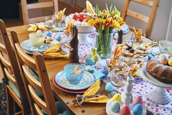 a richly decorated easter table with flowers food and colorful plates and eggs