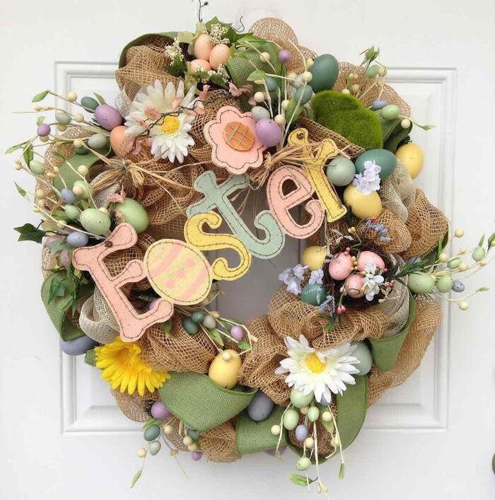 easter wreath with small painted eggs flowers burlap on a white door