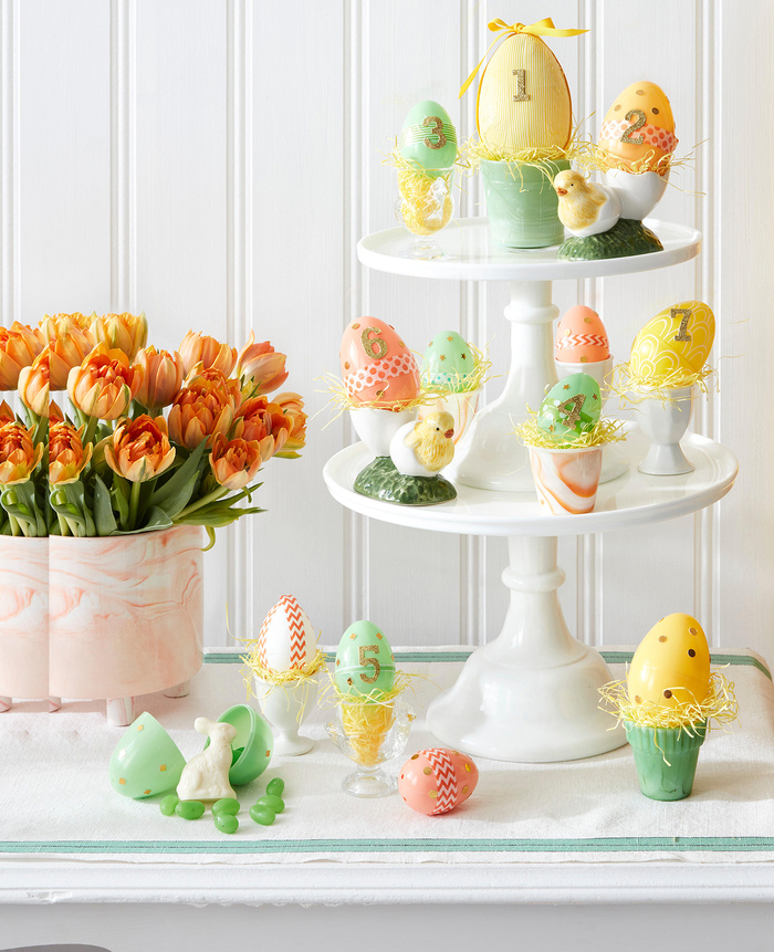 Easter decorations orange tulips in a box and a tall white dessert plate with painted eggs