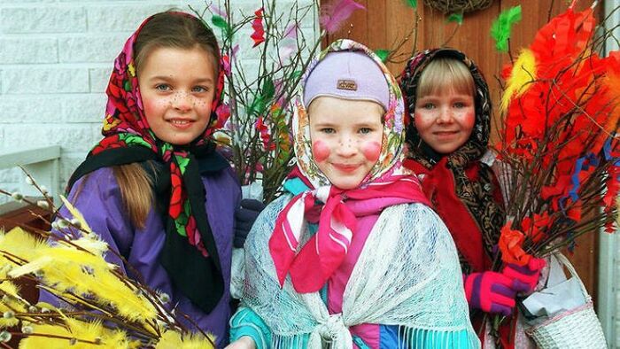 little girls in Finland getting dressed for Easter in traditional costumes three little girls with scarves on their heads holding colorful branches