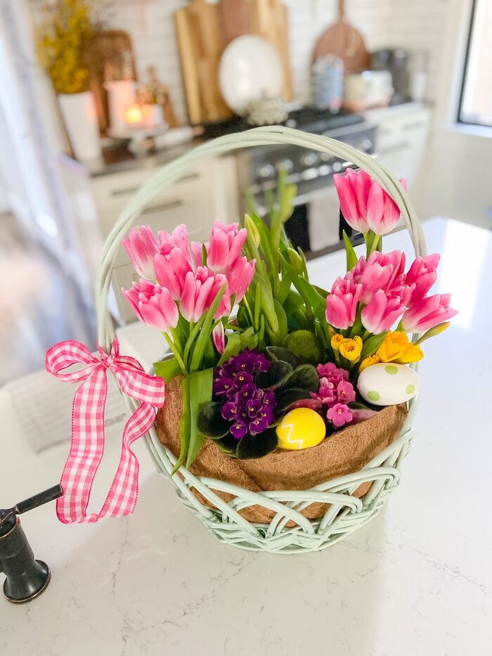 flower basket for Easter in a white kitchen on a white table basket with a pink ribbon and pink tulips