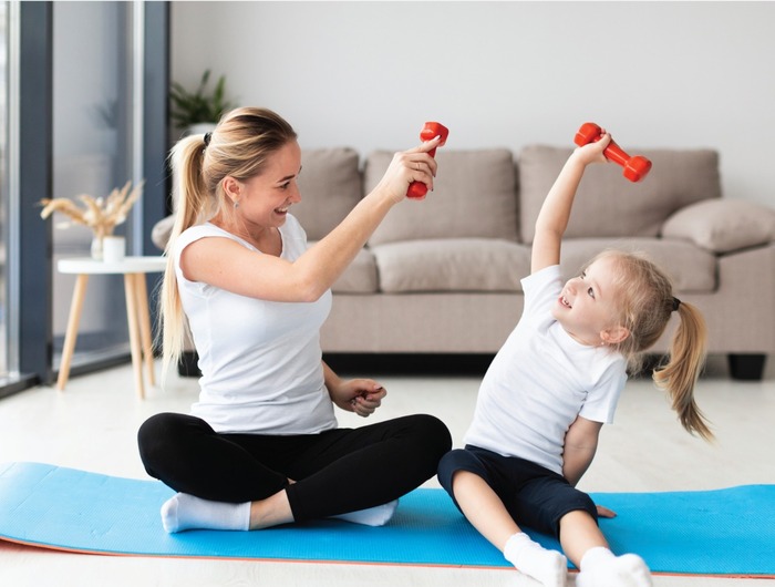 home fitness mommy and daughter on a blue yoga mat with little weights training and playing on the floor