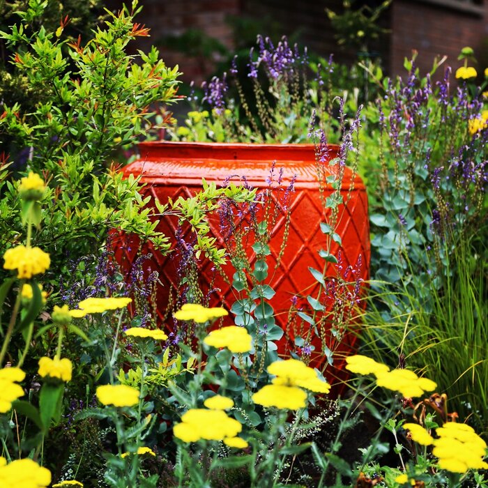 landscape design garden decor a large red container in a garden with flowers blossoming around it