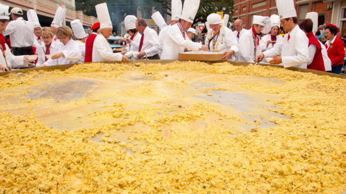 large omelette cooks with tall white hats in front of a huge omelet pan eating and speaking
