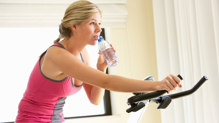 move your body blond woman in a pink sporty outfit working out at home and drinking water from a plastic bottle