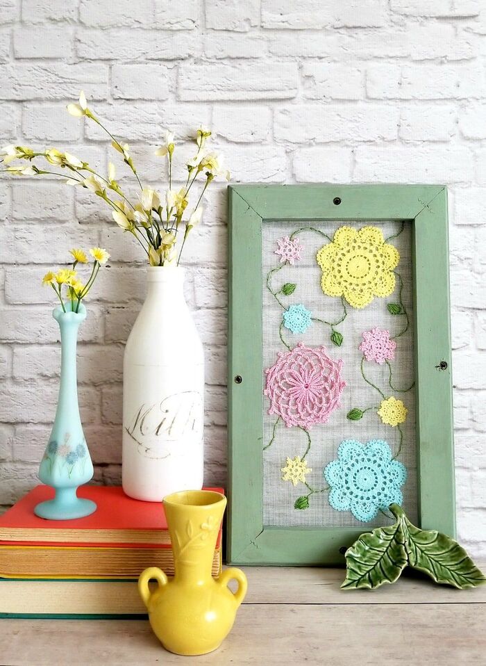 indoors decor embroidery vases in pastel colors on a pile of books on white brick wall