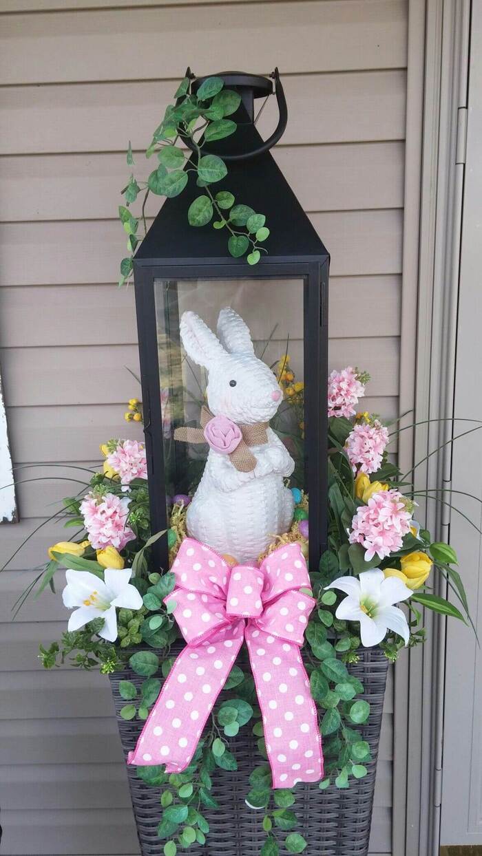 outdoor decor for easter large black lantern with a pink bow and a white bunny inside and flowers outside