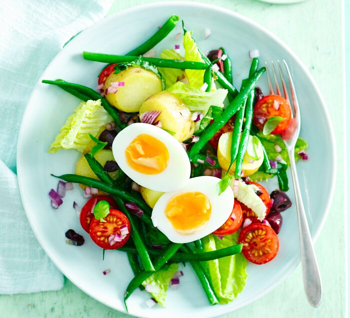 easter salads with egg on top on a light blue bowl and a fork